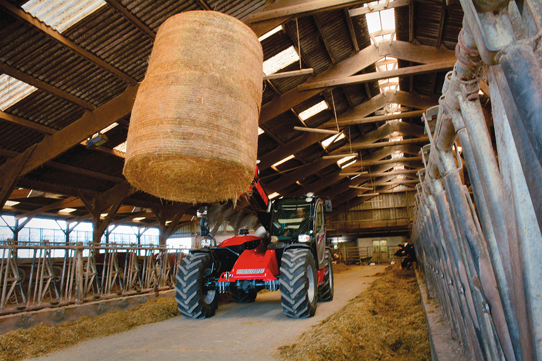 Manitou MLT737 telehandler driving through a cow shed with a raised hay bale